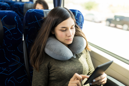 Passenger with comfortable neck pillow using e-book while traveling in busの写真素材