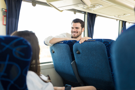 Smiling Latin man looking at friend sitting in busの写真素材