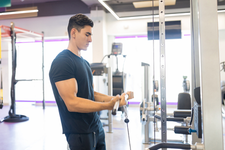 Sportsman in activewear pulling up the handle of fitness equipment while training in gym