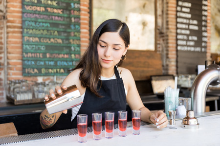 Female bartender pouring alcoholic drink into shot glasses on the bar counter