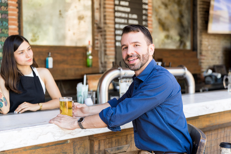 Smiling male customer enjoying beer at counter in restaurantの写真素材