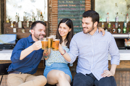 Smiling men and woman toasting alcoholic beverages while sitting in barの写真素材