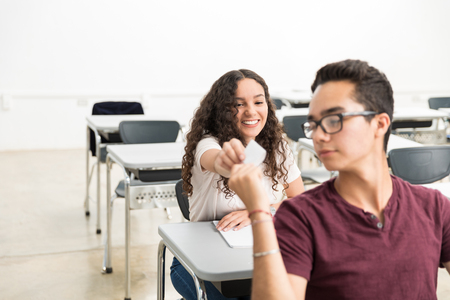 Smiling student giving note to classmate during lecture in high schoolの写真素材