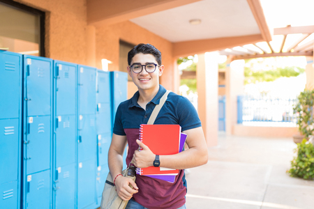 Portrait of cute boy with books and bag standing in college campusの写真素材