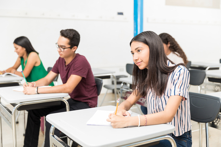 Teenage students writing in books while learning in classroom at high schoolの写真素材