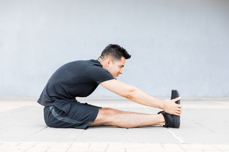 Motivated and concentrated young man stretching foot and doing morning exerciseの写真素材