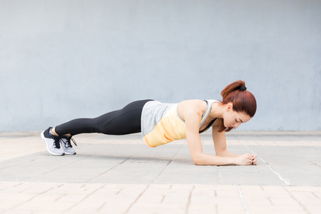 Pretty young woman doing a plank to strengthen her abs on footpathの写真素材