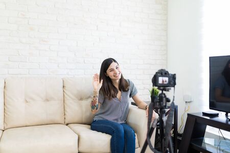 Beautiful video blogger looking at camera and waving to followersの写真素材
