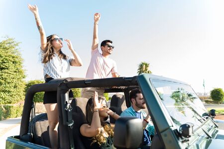 Young friends dancing while riding in 4x4 vehicle against sky