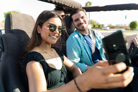 Young woman taking selfie with friends while traveling in SUV