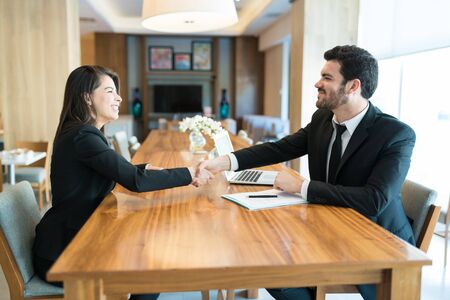 Happy attractive businessman and businesswoman making an agreement with handshake while sitting at...