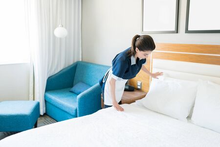 Mid adult chambermaid placing pillows on bed in room at hotelの写真素材
