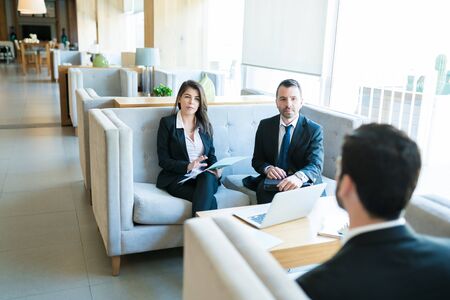 Confident business colleagues taking interview of candidate while sitting in lobby at hotelの写真素材