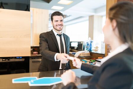 Attractive male Hispanic clerk giving credit card back to female executive at counter in reception...