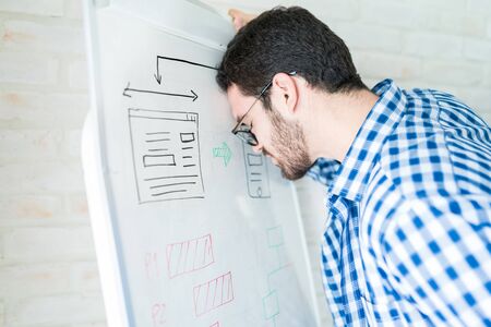 Stressed businessman leaning on whiteboard in meeting room at office