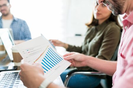 Businessman analyzing graphs while sitting with colleagues in meeting at office
