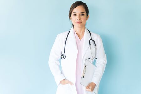 Good looking medical professional with stethoscope and clipboard against plain backgroundの写真素材