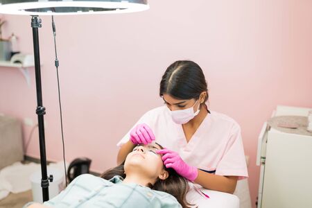 Young cosmetician treating woman's eyes at beauty salonの写真素材