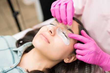 Latin female customer getting perfect eyelashes during treatment at salon