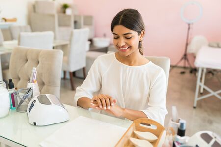 Satisfied female client looking at manicured fingernails after treatment in spa