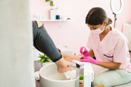 Young beautician grooming client's toenails during pedicure at spaの写真素材