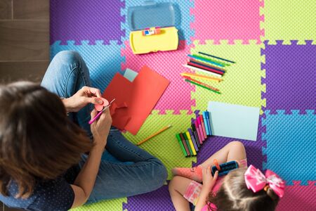 High angle view of mother assisting little daughter with craft work at homeの写真素材