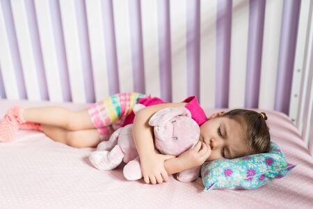 High angle view of little girl sleeping with teddybear on bed at homeの写真素材