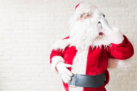 Male Santa Claus looking away while talking through mobile phone and standing at homeの写真素材