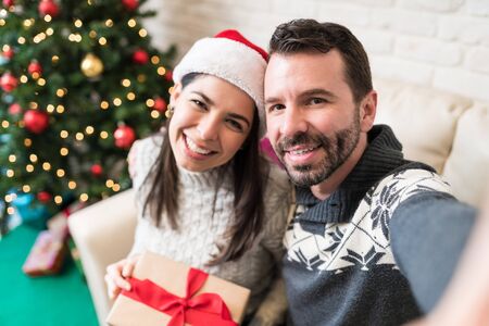 Cheerful couple taking selfie while enjoying Christmas holiday at home