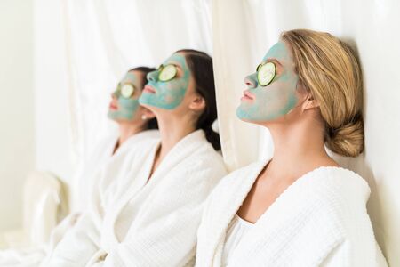 Female friends relaxing with cucumber and facial masks while sitting in beauty spaの写真素材