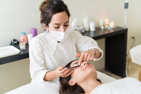 Female Caucasian cosmetician brushing Hispanic customer's eyelash at healthcare centerの写真素材