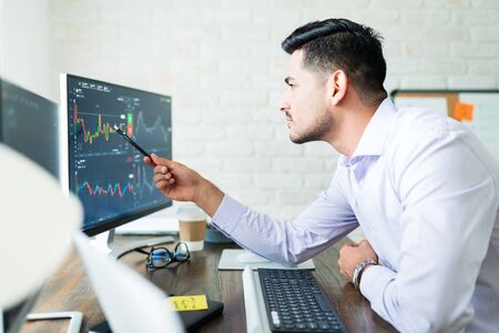 Dedicated attractive finance professional analyzing share graph from computer screen at desk while...