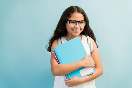 Portrait of smiling female student wearing eyeglasses while holding books in studio