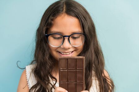 Closeup of cute girl tempted while looking at chocolate bar against turquoise backgroundの写真素材