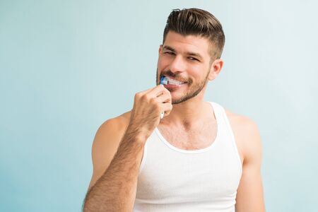 Portrait of young handsome Hispanic man brushing teeth  in studioの写真素材