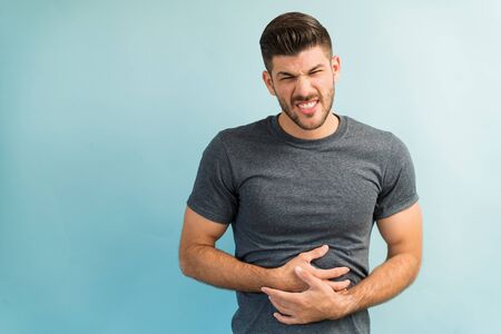 Young male with stomachache frowning against plain background