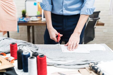 Midsection of young tailor cutting fabric with scissors on workbench in textile industry