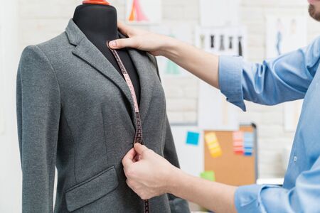 Cropped image of dressmaker using tape measure on mannequin with suit at fashion studioの写真素材