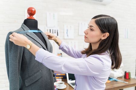 Young Hispanic designer measuring suit on dummy at design studioの写真素材
