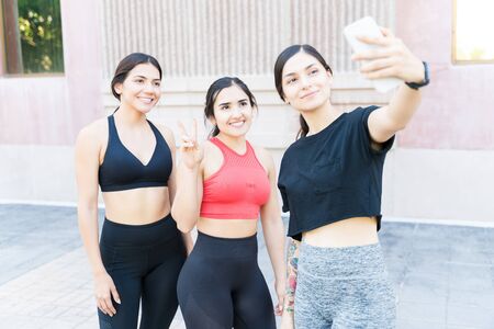 Beautiful Hispanic woman taking selfie with Caucasian friends while standing in city