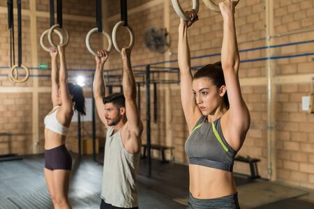Young male and female athletic friends using gymnastic rings during cross training at gym
