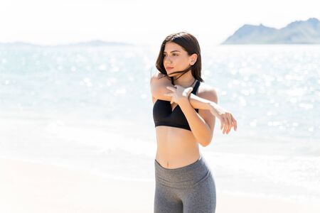 Determined young woman stretching arm while standing on beach
