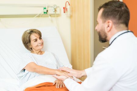 Smiling senior patient looking at doctor giving support to her during treatment in hospitalの写真素材