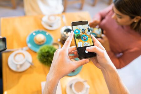 Man photographing dessert and coffee on smartphone while enjoying with friends at cafe