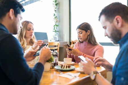Distracted male and female friends using smartphones while sitting together at restaurantの写真素材
