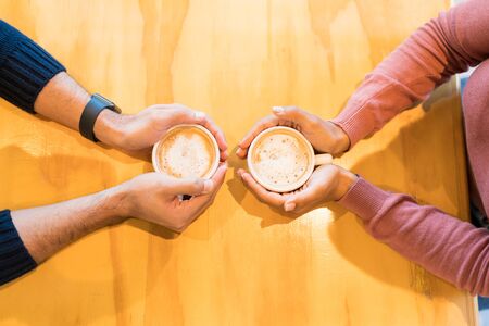 Overhead view of couple holding coffee cups while sitting together at table in cafeの写真素材