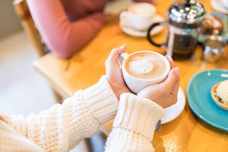 Midsection of woman holding coffee cup while sitting with friend at cafeの写真素材