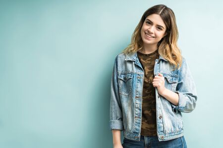 Portrait of stylish smiling woman wearing denim jacket standing against colored backgroundの写真素材