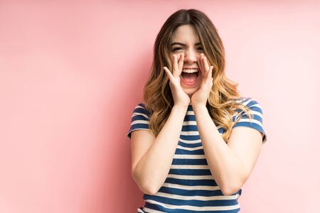 Excited cheerful woman shouting with open mouth while standing against coral background in studio