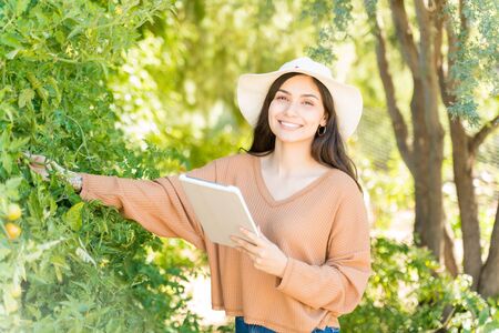 Portrait of smiling female farmer with digital tablet standing by plants in farm